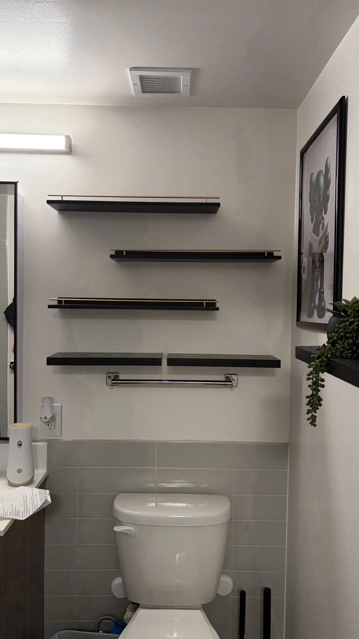 Black floating shelves and a towel bar installed on a tiled bathroom wall above a toilet