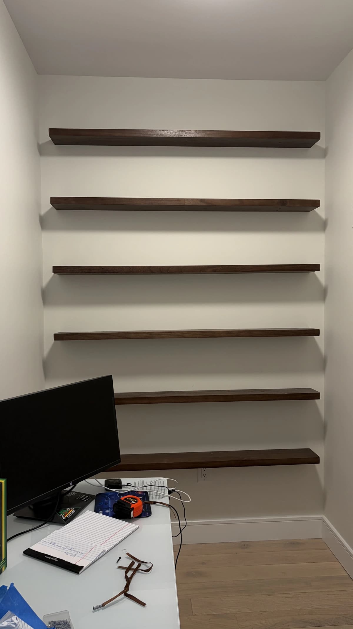 Six dark wood floating shelves installed across a home office wall