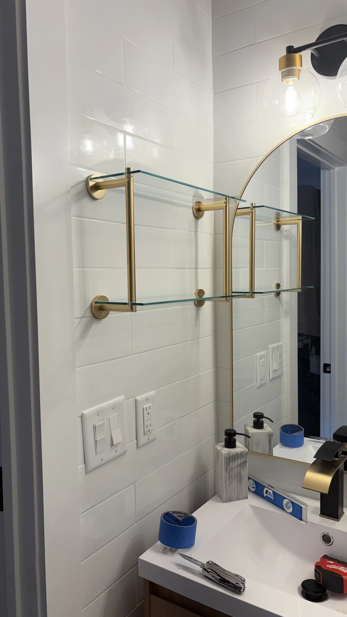 Gold-bracket glass bathroom shelves mounted beside a vanity mirror