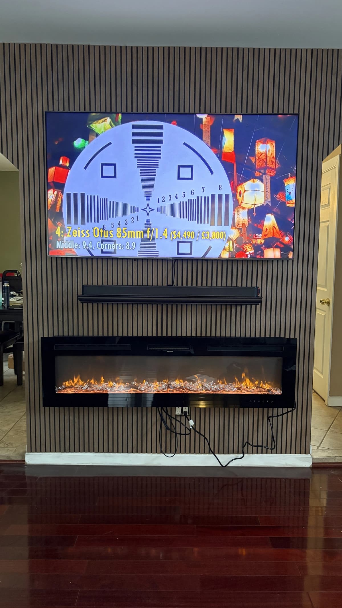 Wall-mounted flat-screen TV with a soundbar on a slatted accent wall above an electric fireplace